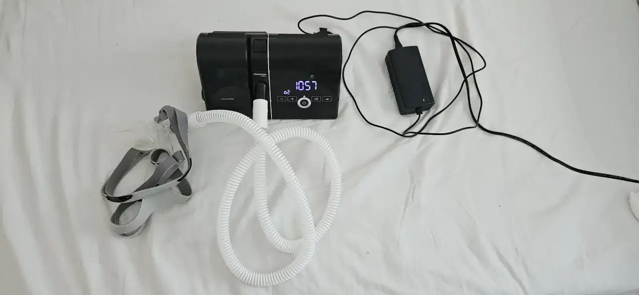 A CPAP machine on a white sheet with its hose, mask and power supply.