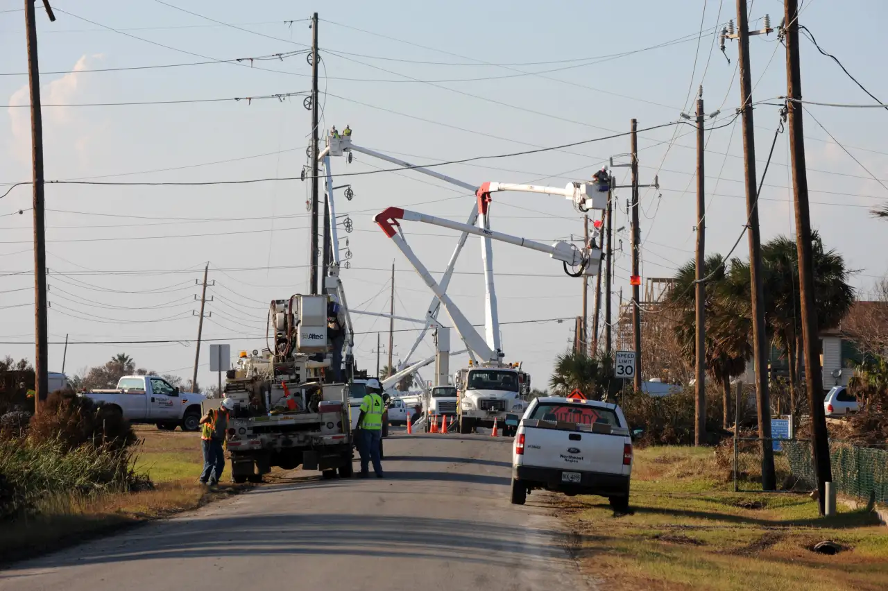 Utility crews in bucket trucks repairing power lines along a road on Galveston Island.